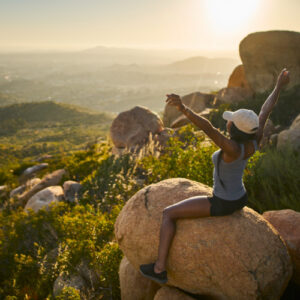 san diego naturopathic doctors smiling woman sitting ontop boulder on mountin hands in air