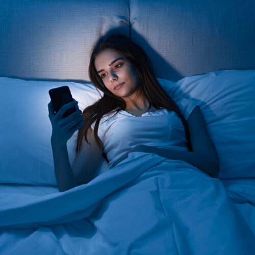 san diego naturopathic doctors woman laying in bed staring at bright smart phone